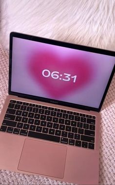 an open laptop computer sitting on top of a white bed next to a pink heart