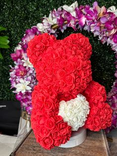 a teddy bear made out of flowers sitting on a wooden table next to purple and white flowers