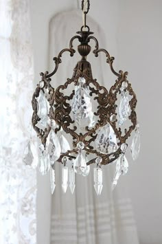 a chandelier hanging from the ceiling in front of a window with white curtains