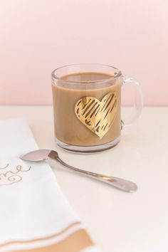 a cup of coffee with a gold heart on the side and spoon next to it