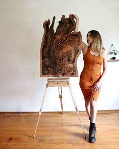 a woman in an orange dress is standing next to a large piece of art on a easel