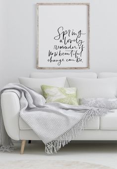 a white couch with a blanket on it in front of a framed quote above it