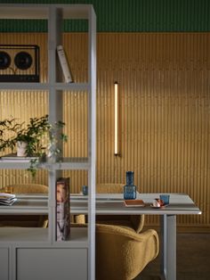 a table with two chairs and a plant on it in front of a wall that has vertical blinds