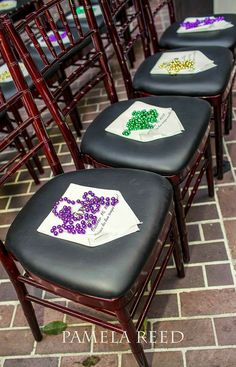 four black chairs with purple and green flowers on them, sitting side by side in front of a brick floor