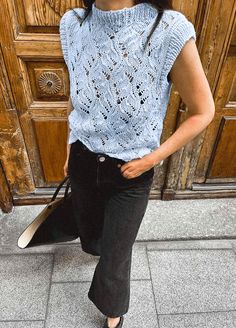 a woman standing in front of a wooden door wearing black pants and a blue top