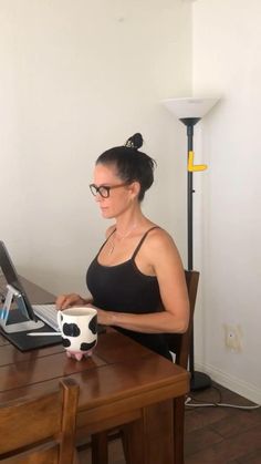 a woman sitting at a table with a laptop computer and cow mug in front of her