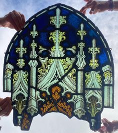 four hands holding up a stained glass window in front of a cloudy blue and white sky