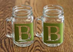 two glass mugs sitting on top of a wooden table with letters painted on them