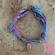 a pink and blue bracelet with an initial charm on the clasp, sitting on a stone surface