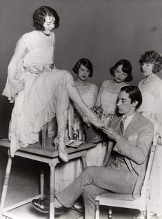 an old black and white photo of four women sitting around a man in a suit