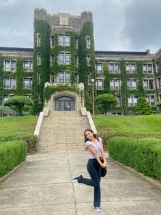 a woman standing in front of a large building with ivy growing on it's walls