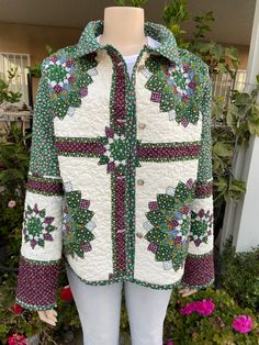 a green and white quilted jacket with flowers on the front, sitting next to some pink flowers