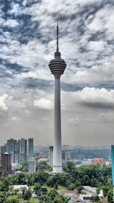 a tall tower towering over a city under a cloudy sky with buildings in the background