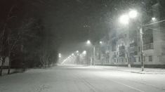 an empty street at night with snow on the ground and lights shining in the dark