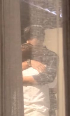 a man and woman embracing each other in front of a window with the reflection of them