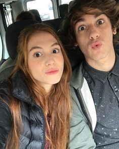 a young man and woman sitting in the back seat of a car with their eyes wide open