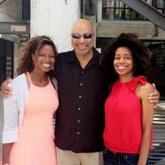 three people standing next to each other in front of a building and smiling for the camera