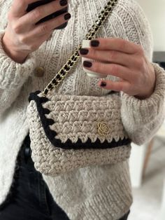 a woman is holding her purse and looking at her phone while wearing black nail polish