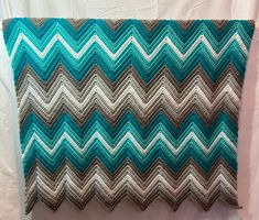 a crocheted blanket is sitting on a white bed sheet with blue and gray chevrons