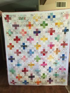 a woman holding up a large quilt made with squares and crosses on the front, while standing next to a wooden floor