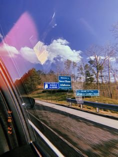 the view from inside a car looking at highway signs and trees on either side of the road