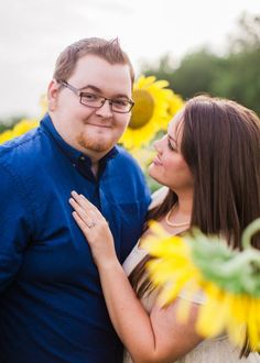 a man and woman standing next to each other with sunflowers in the background