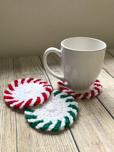 two crocheted candy cane coasters sitting next to a coffee cup