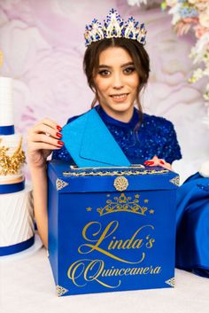 a woman in a tiara holding up a blue box with the words linda's quinceauera written on it