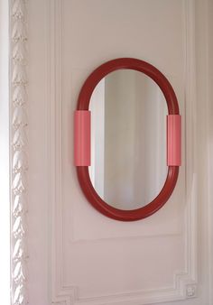 a round mirror mounted to the side of a white wall next to a red door