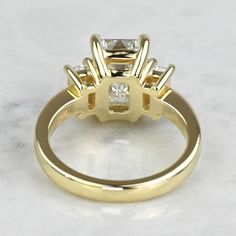 a yellow gold engagement ring with three princess cut diamonds on the side and four prongs