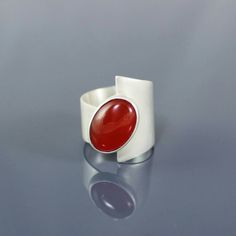 Modernist Carnelian Statement Ring This bold modernist style ring features a beautiful Carnelian gemstone set on a wise brushed sterling silver band. The gem is a vivid burnt orange/ light red colour and measures 14mm x 10mm. The band is 0.8 mm thick and measures of 21mm at the tallest end tapering to 9.5mm. I only use Sterling silver. This ring tested for quality and stamped with my makers mark at the Londan Assay Office, Goldsmiths Hall where I am professionally registered.  UK size M, please Modern Wide Band Ring As Gift, Handmade Oval Moonstone Ring In Modern Style, Modern Handmade Oval Moonstone Ring, Handmade Modern Oval Moonstone Ring, Modern Wide Band Ring For Wedding, Modern Bypass Ring For Anniversary, Modern Red Cabochon Ring, Contemporary Gemstone Rings For Gifts, Contemporary Gemstone Rings For Gift