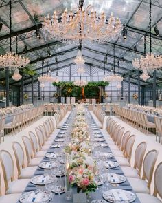 a long table set up with plates and silverware for a formal dinner in a greenhouse