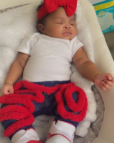 a baby sleeping in a white chair with a red bow on it's head