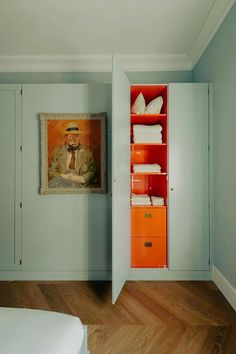 a bedroom with blue walls and wooden flooring has an orange bookcase in the corner