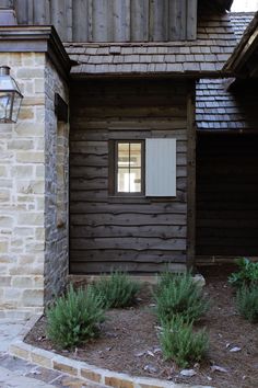 a small wooden building with a window and some plants in front of the door area