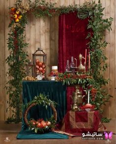 an arrangement of fruit and flowers on display in front of a wooden wall with red curtains