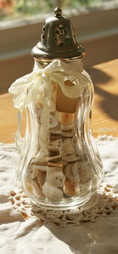 a glass jar filled with seashells on top of a white lace covered table cloth