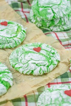 some green and white cookies with red hearts on them are sitting on a tablecloth