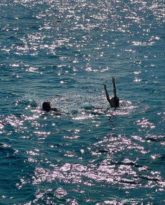 two people swimming in the ocean with their hands up and one person diving into the water