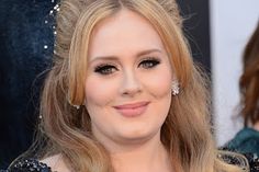 a woman with long blonde hair and black eyeshadow smiles at the camera while standing in front of an oscars red carpet