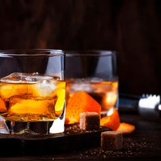 two glasses filled with ice and orange peels on top of a wooden table next to a bottle of booze