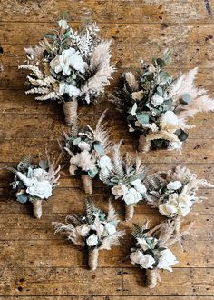 several bouquets of flowers are arranged on a wooden table with dried grass and feathers