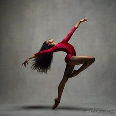 a woman in a red leotard is doing a dance move with her arms outstretched