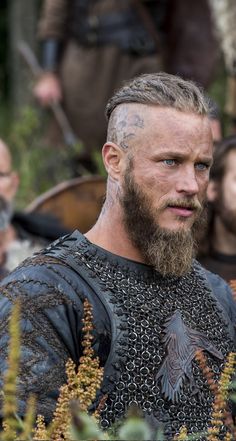 a man with tattoos on his face and chest standing in front of other men wearing armor