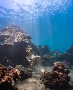 a woman sitting on the bottom of a rock under water