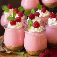 small desserts with whipped cream and raspberries on a wooden tray next to spoons