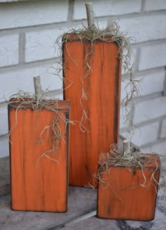 three wooden pumpkins sitting on top of a table next to a brick building with vines growing out of them