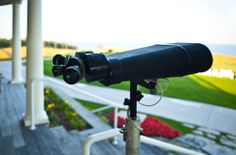 a telescope is sitting on top of a tripod near the grass and flowers outside