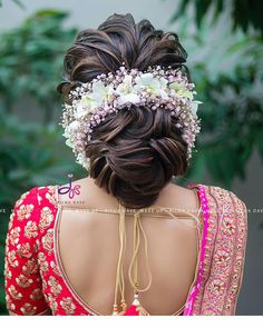 the back of a woman's head with flowers in her hair, wearing a red and pink saree