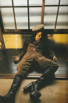 a man sitting on top of a wooden bench wearing black boots and a fedora